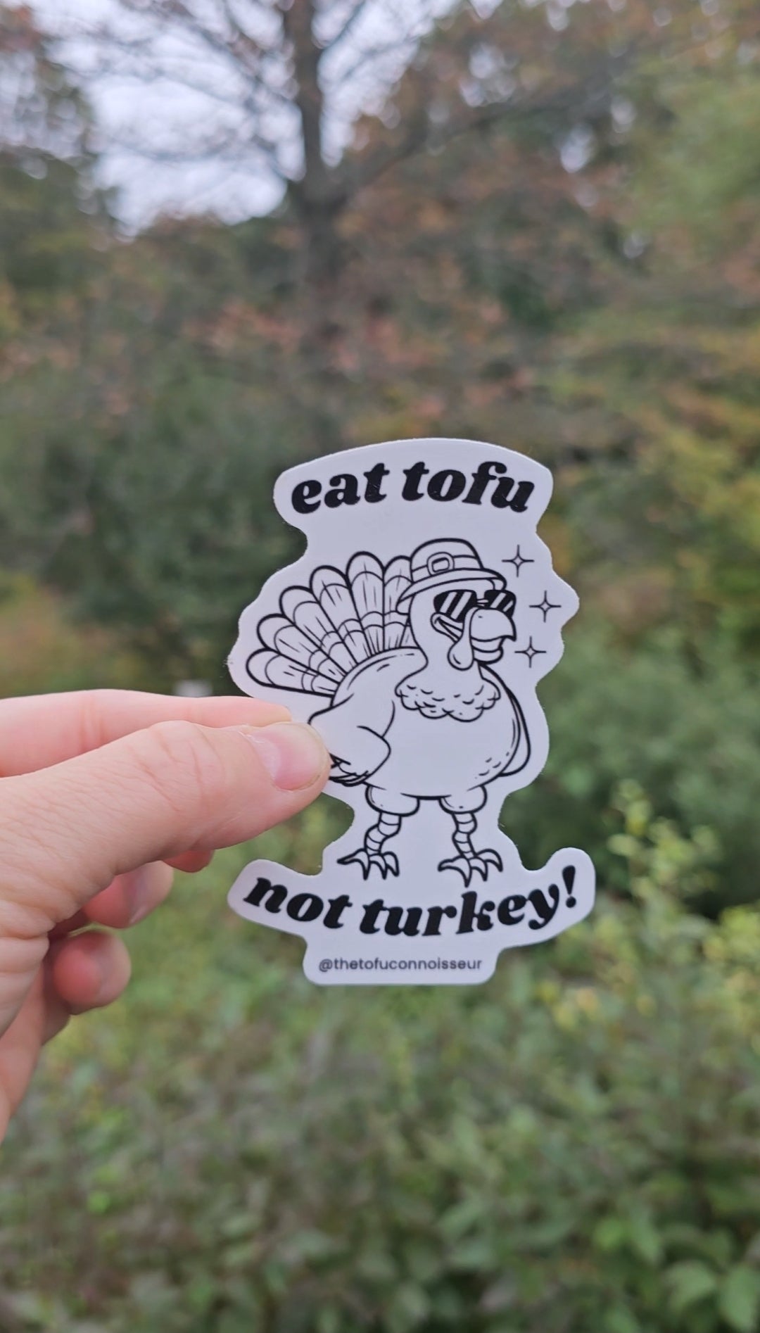 Sticker with a turkey graphic and text held by a hand against a blurred natural background